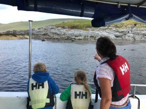 Family on Skellig Michael boat tours, viewing the island's rugged coastline and wildlife from the boat. Safety first, wearing life vests. 