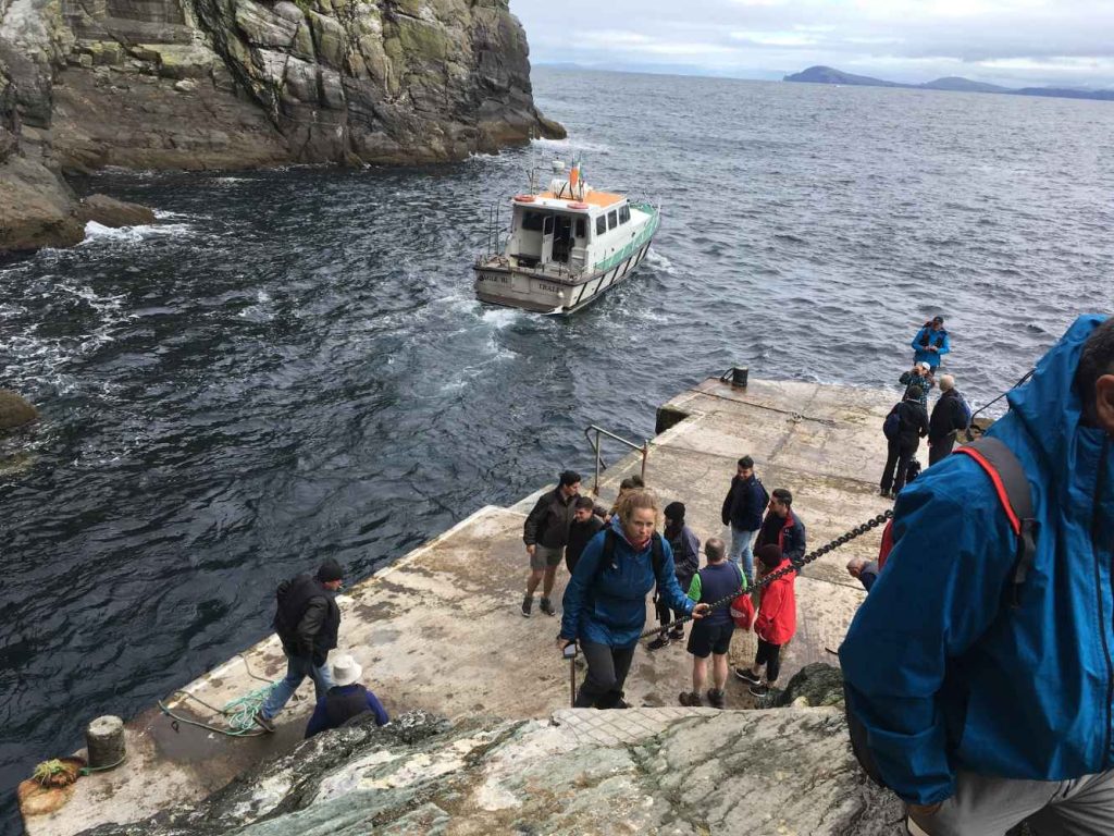 Tourists disembarking from a boat at Skellig Michael. Steps lead up to the island, showcasing the rugged terrain. Full stop.